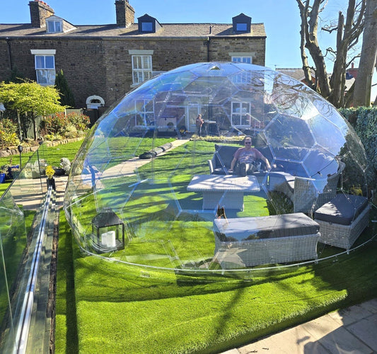 A GeoDomeX dome on a lawn beside a stone house