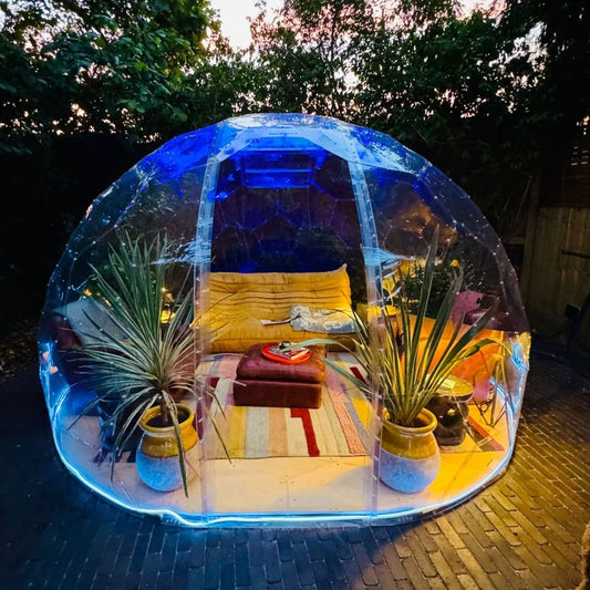 A GeoDomeX dome filled with plants, cushions and rugs, lit at night
