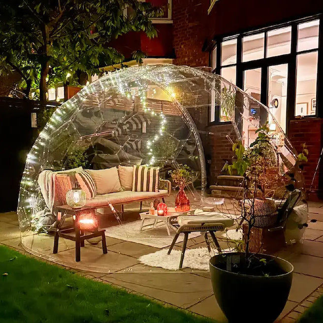 A GeoDomeX dome glowing with warm lights in a garden at dusk