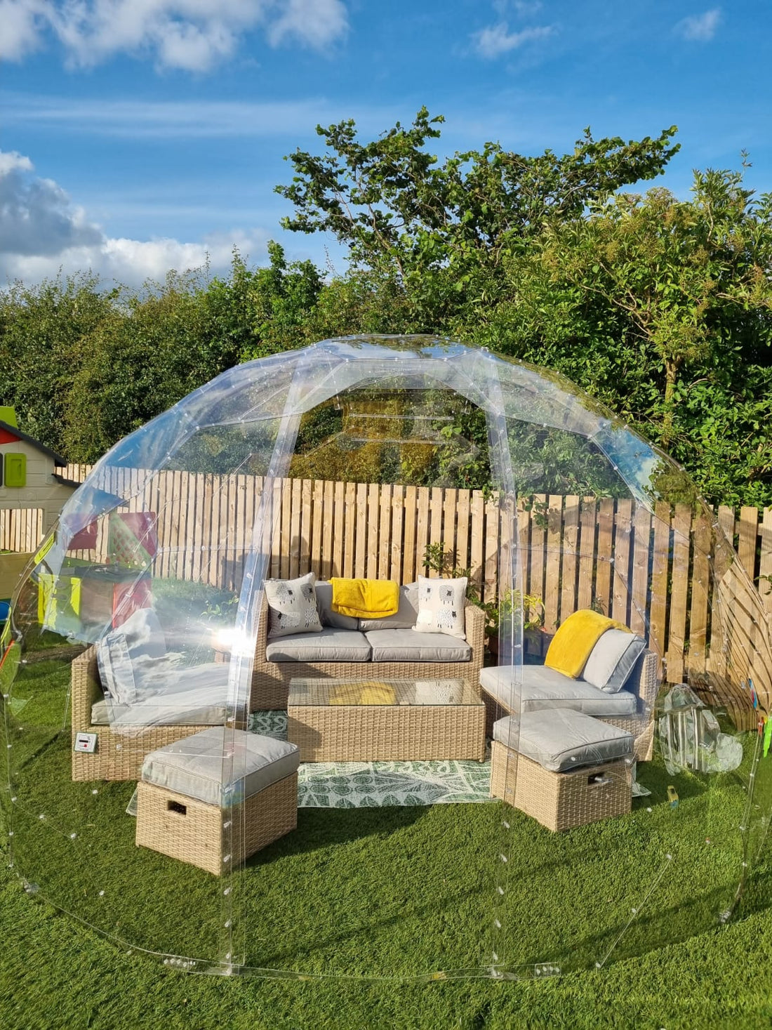 A GeoDomeX dome with rattan sofas on a lawn on a sunny day